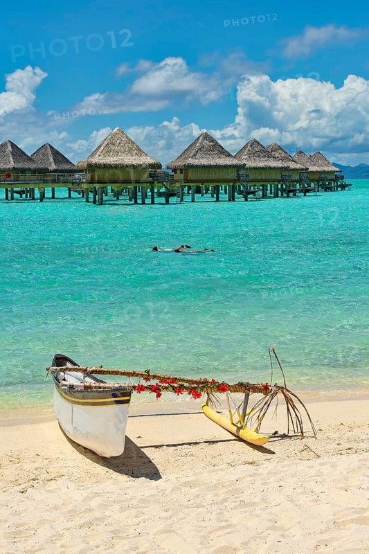 Decorated outrigger boat in front of overwater bungalows