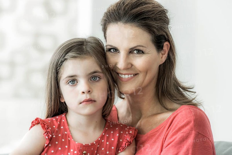 Mother and daughter sit together on the couch and look into the camera