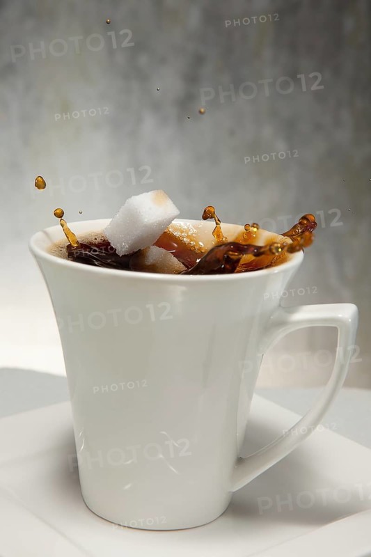 Two sugar cubes falling into a cup of coffee
