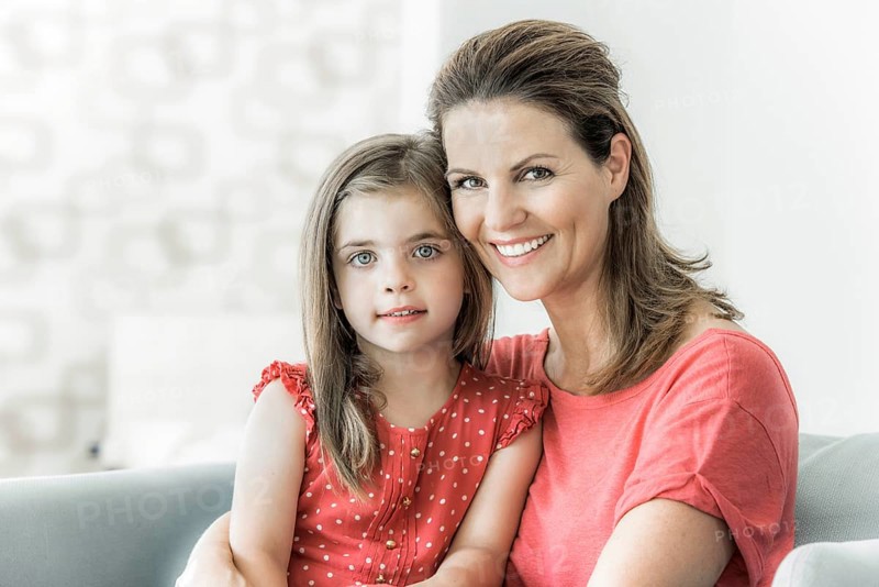 Mother and daughter sit together on the couch and look into the camera