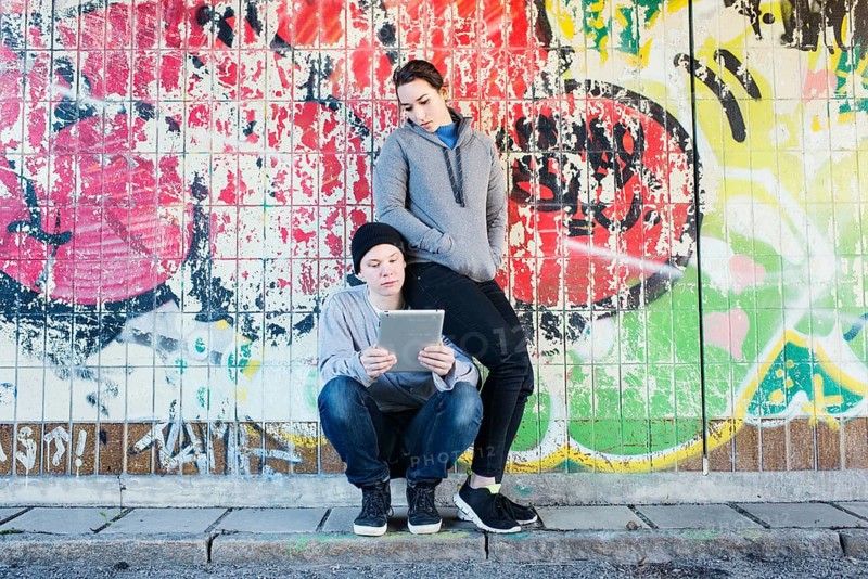 Casual and relaxed young man and woman reading on a notepad in front of grafitti wall in urban area