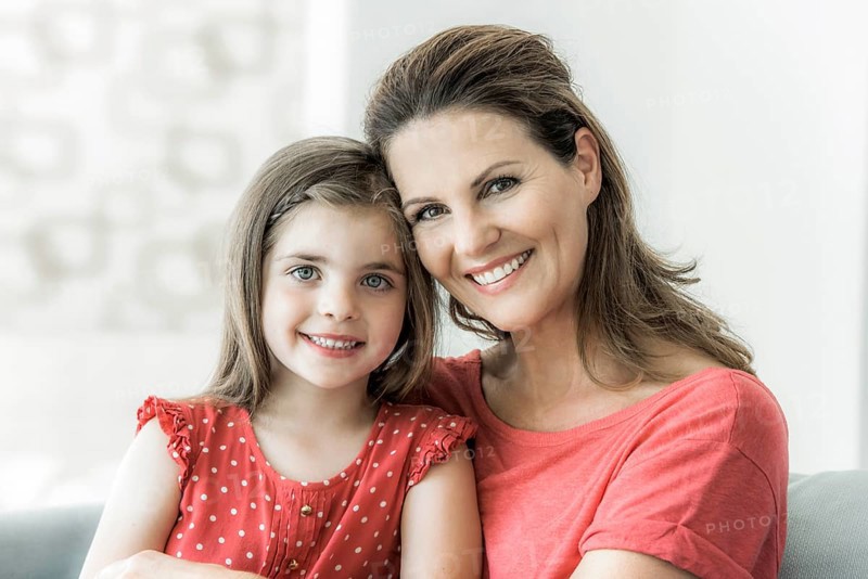 Mother and daughter sit together on the couch and look into the camera