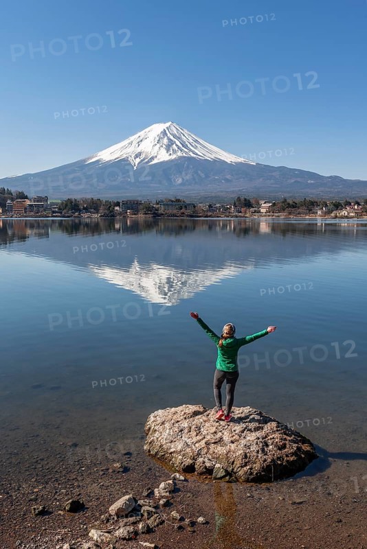 Young woman stands on stone in the water and stretches arms into the air