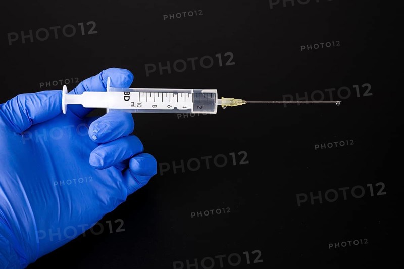 A hand with a blue medical glove is holding a syringe