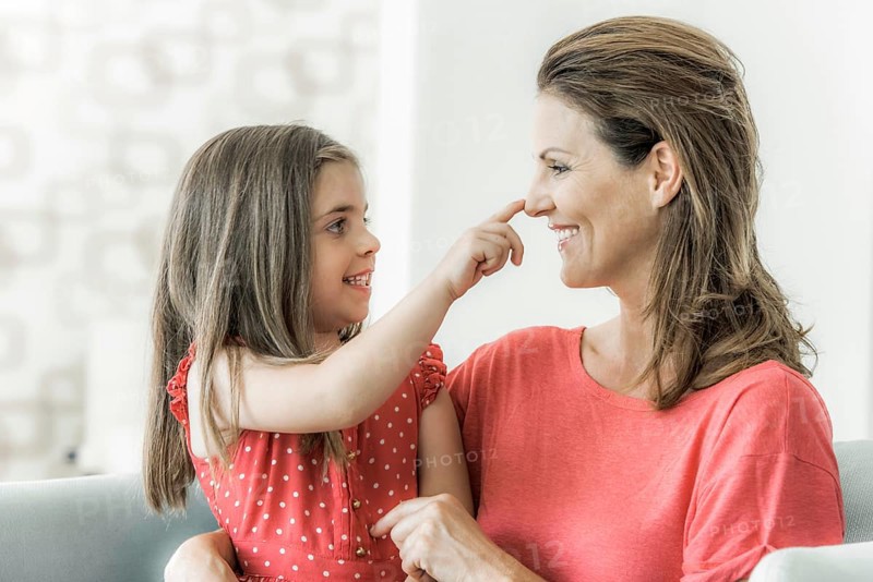 Mother and daughter sit on the couch together and look at each other