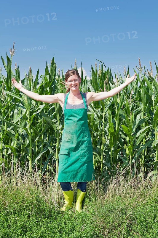 Young woman in work clothes standing with outstretched arms in front of a maize field