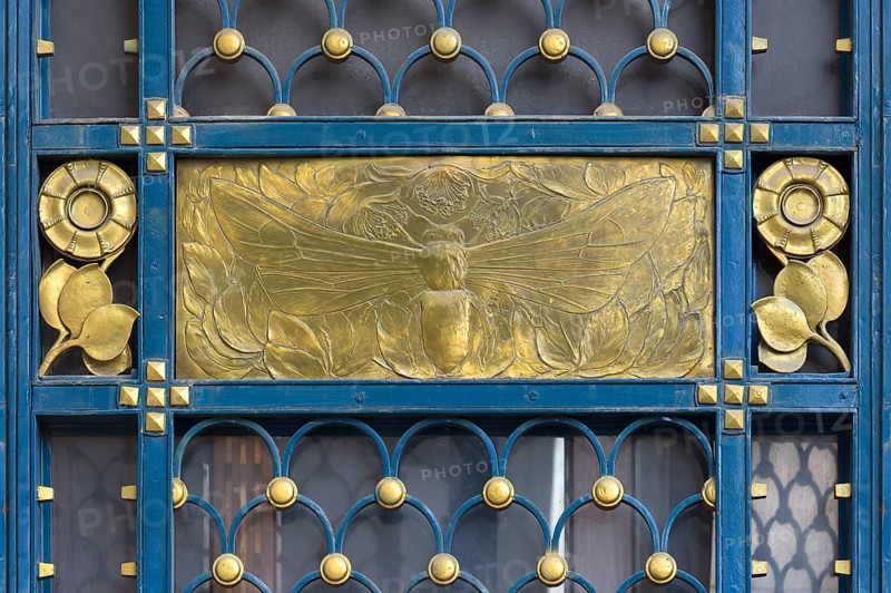 Gold-coloured relief of a bee at a wrought-iron gate around 1900