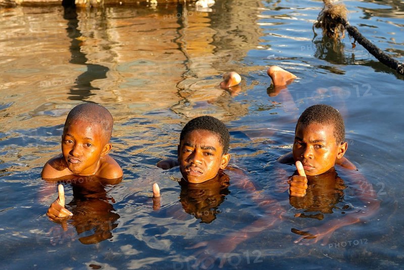 Three boys in the water showing a thumbs up