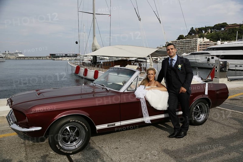 Bride and groom posing with an open Ford Mustang convertible car at a harbour