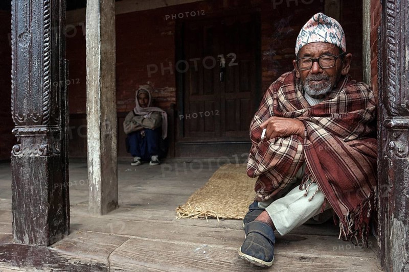 Nepalese man wrapped in a blanket sitting at an entrance