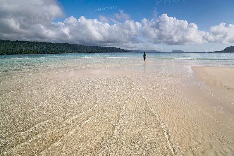 Woman walking across a sandbank to the beach