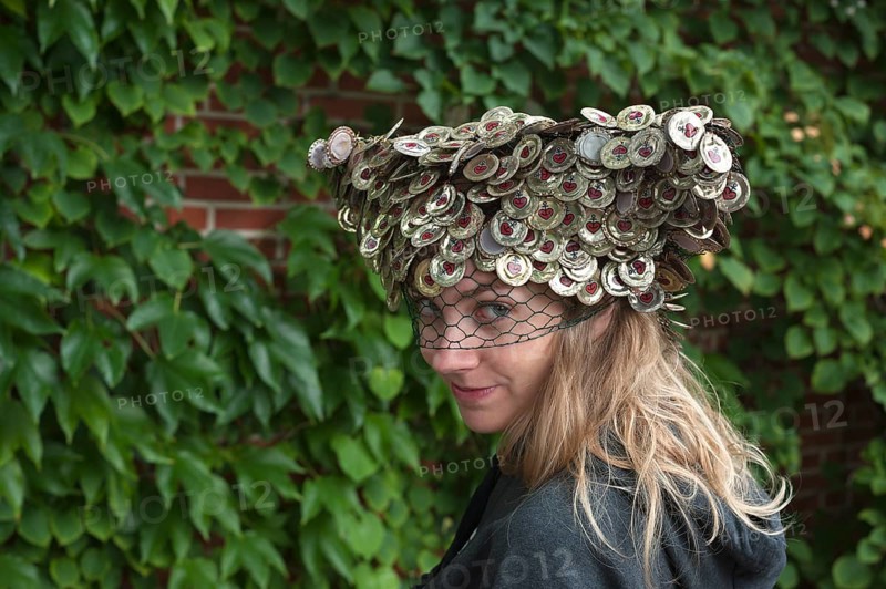 Young woman wearing a hat made of crown corks in front of a wall of leaves
