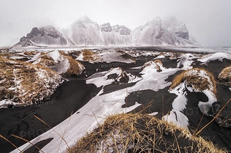 Snow on black sand dunes in front of Vestrahorn mountain in winter
