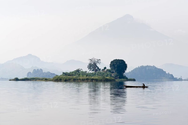 Canoe glides in the morning mist on Mutanda Lake in front of Muhavura volcano at the border with Rwanda