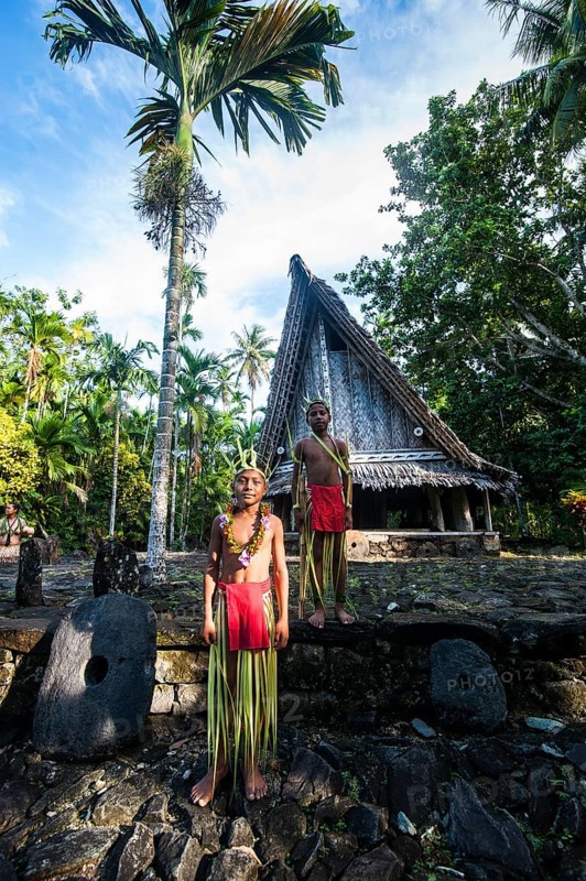 Two traditionally dressed boys standing in front of a traditional hut