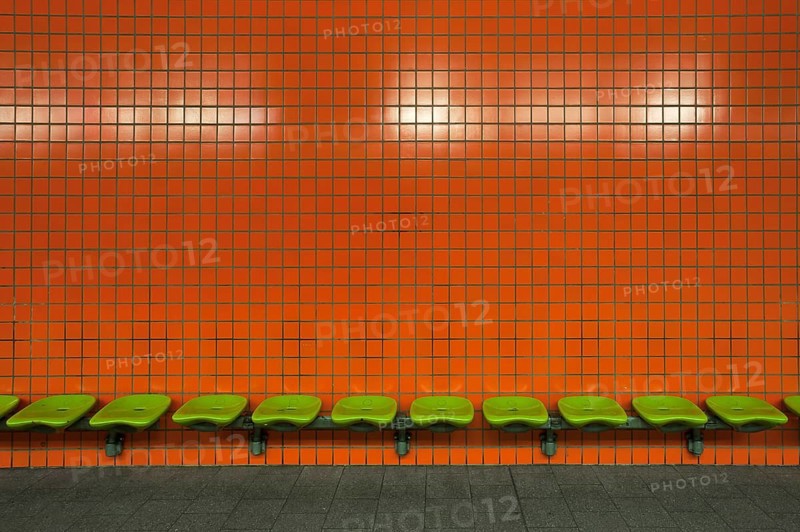 Green seats in front of an orange tiled wall in an underdground station