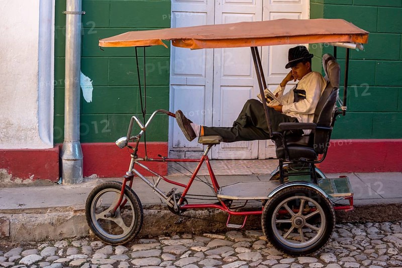 Rickshaw driver waiting for customers and reading a book