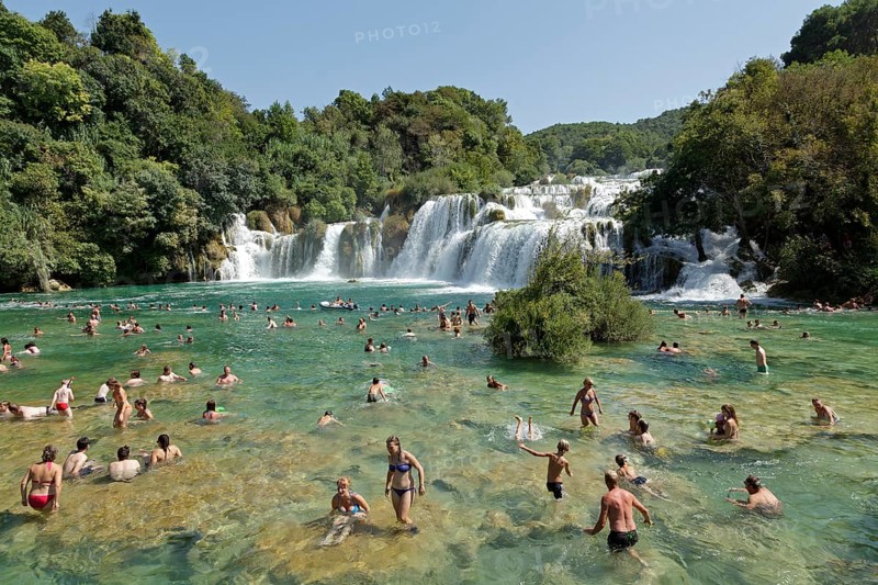 People swimming in front of a waterfall