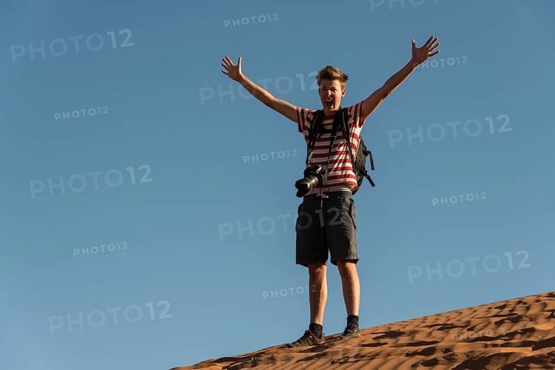 Teenager with photo camera standing on a dune and spreading his arms