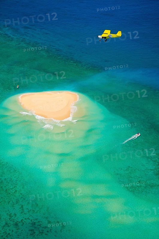 Small plane flying over coral reef with sand island