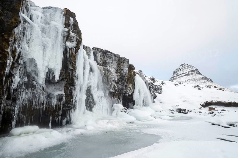 Mountain Kirkjufell behind frozen waterfall Kirkjufellsfoss in the snow