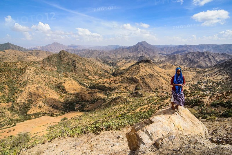 Local woman standing on a rock in front of the mountain scenery along the road from Massawa to Asmarra
