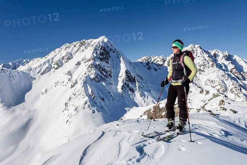 Ski tourer on the summit of Mt Seespitz in the Deutschnonsberg area with the mountains Illmenspitz and Proves at the back