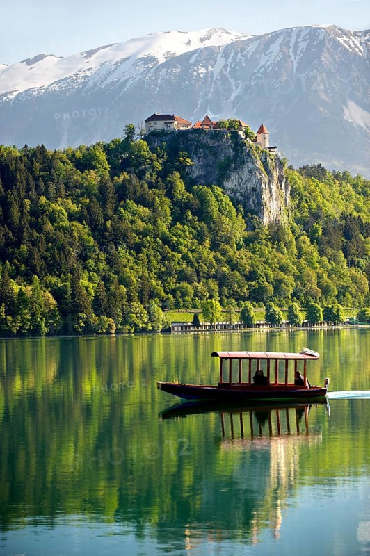 A flat bottomed boat called Pletna on Lake Bled with Bled Castle and the alps at the back