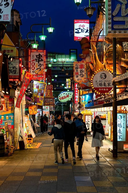 Many colorful neon signs in a pedestrian zone with shops and restaurants