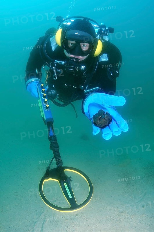 Diver with metal detector displaying found ancient coins