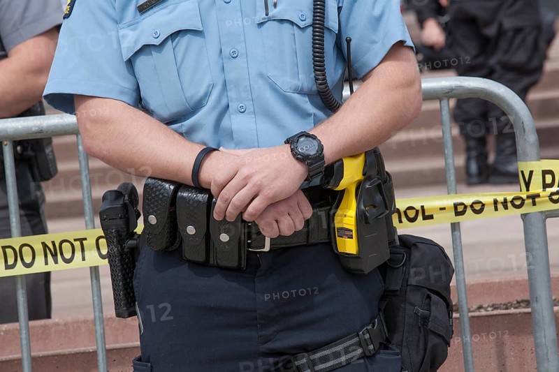 Policeman carries a gun on his right and a taser on his left