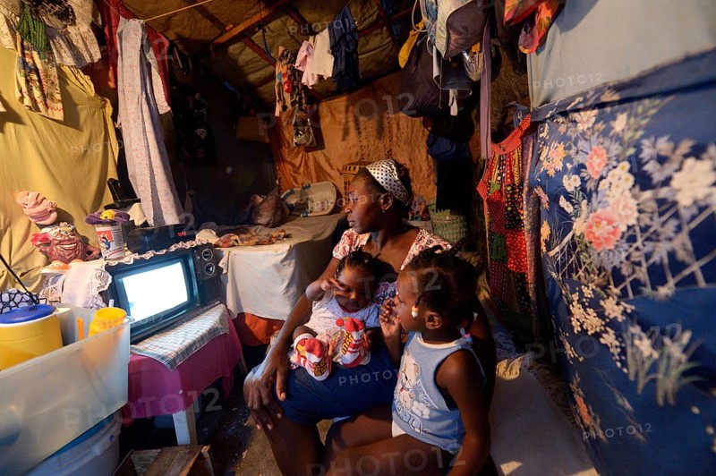 Woman with two children watching television in a shack
