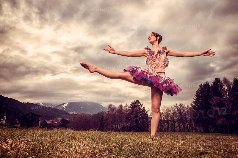 Ballerina wearing a tutu dances in front of a cloudy sky