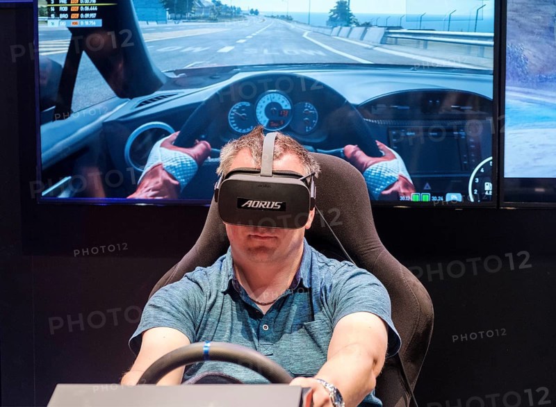 Visitor wears Virtual Reality glasses in a driving simulator for car racing at gamescom