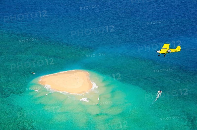 Small plane flying over coral reef with sand island