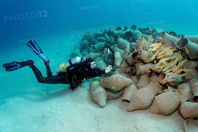 Underwater photographer photographing school of fish on amphora