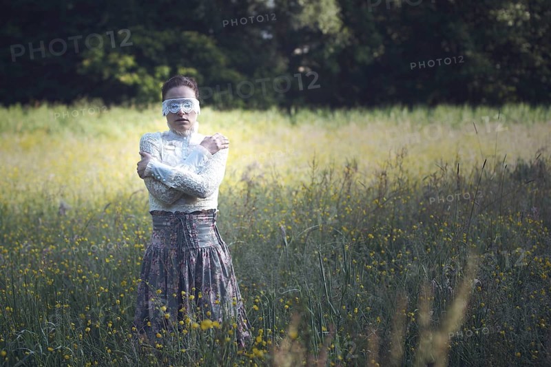 Woman with a lace mask in front of her eyes standing in a meadow