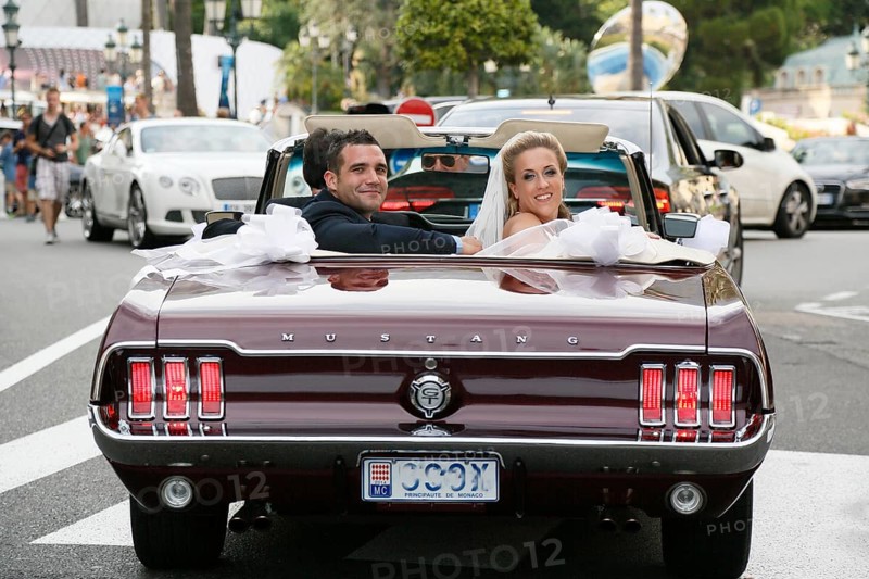 Bride and groom riding in an open Ford Mustang convertible car through the city
