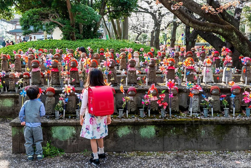 Two schoolchildren in front of Jizo statues with red caps