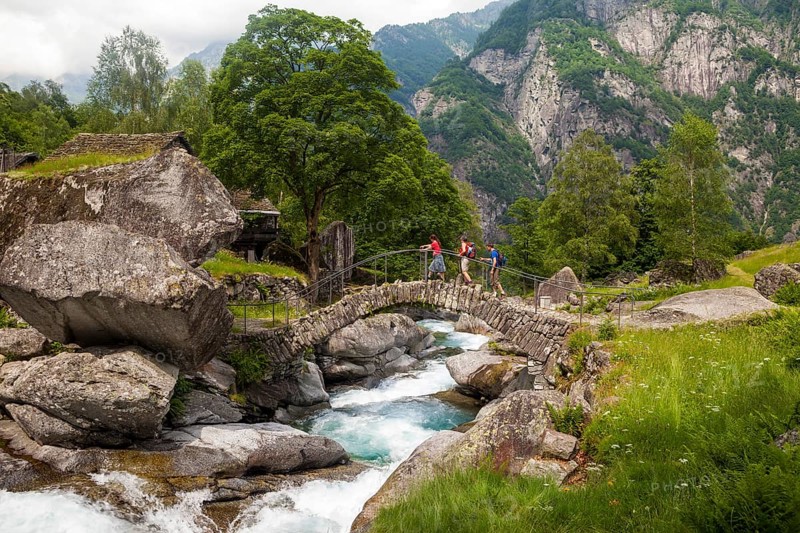 Three hikers crossing a medieval arch bridge