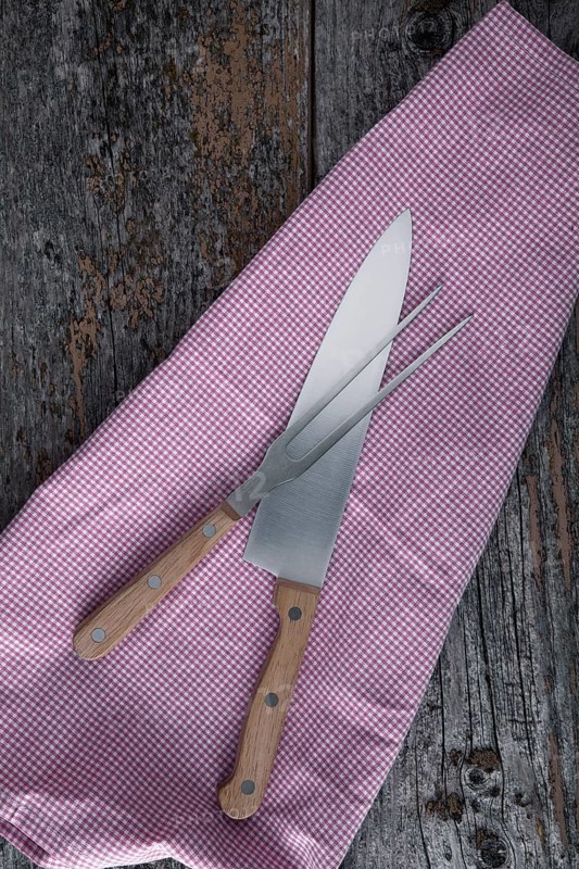 Carving knife and fork with a kitchen towel on rustic wooden boards