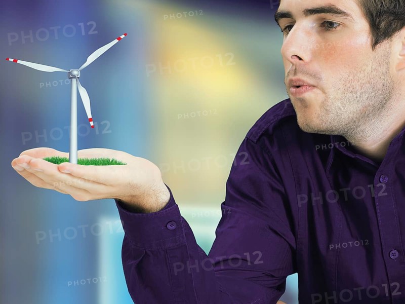 Man blowing a miniature wind turbine in his hand