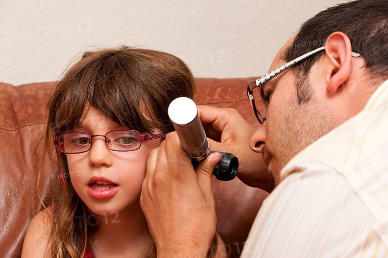 Doctor during a home visit examining a girl with an otoscope