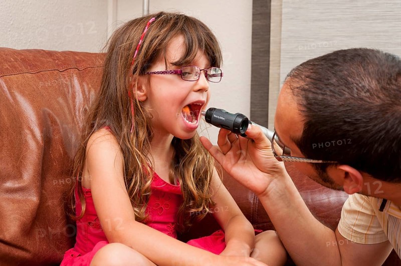 Doctor during a home visit examining a girl with an otoscope