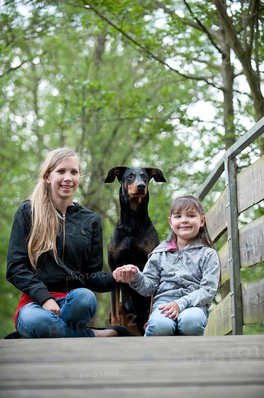 Two girls sitting with a Doberman on a bridge