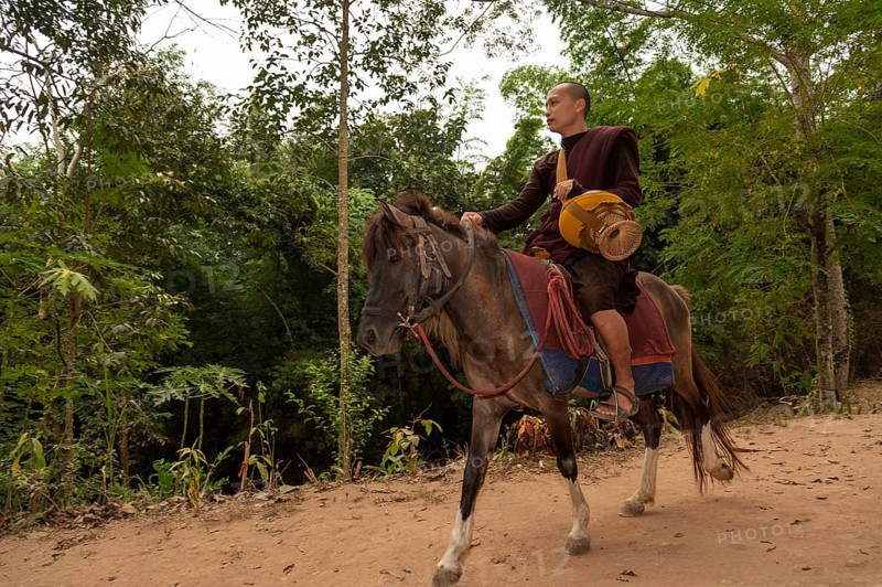 Buddhist monk on horseback with a begging bowl collecting alms in the morning