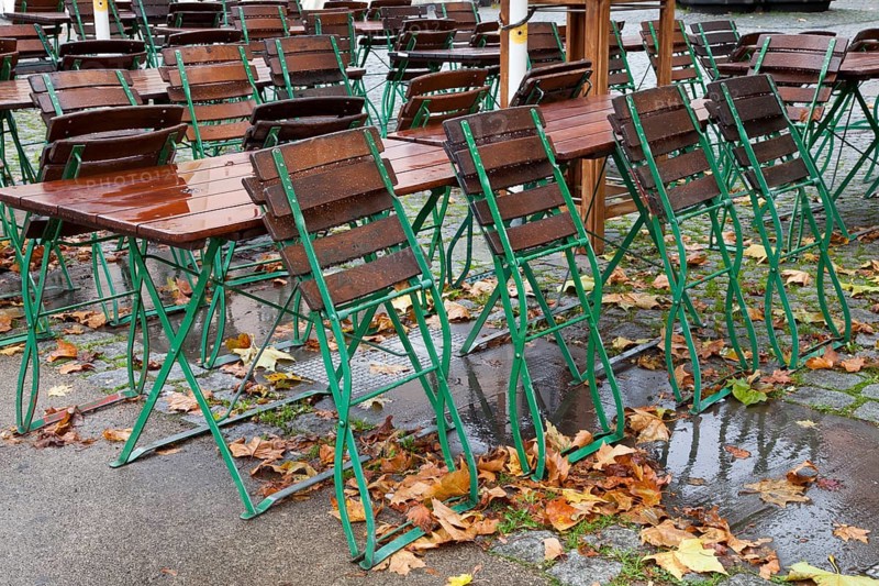 Empty tables and chairs of an outdoor restaurant in the rain with autumn leaves in the historic city centre of Cologne