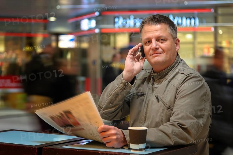 Man with a newspaper and a mobile phone in a shopping mall
