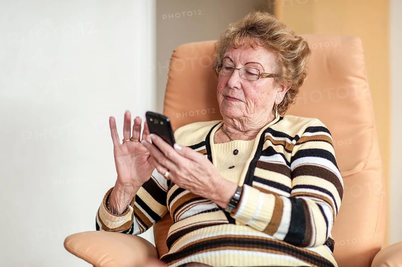 Elderly woman sitting in an armchair and using a smartphone