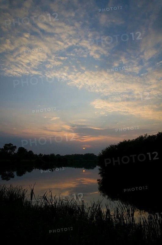 View of cirrocumulus clouds over flooded former gravel pit habitat at sunset